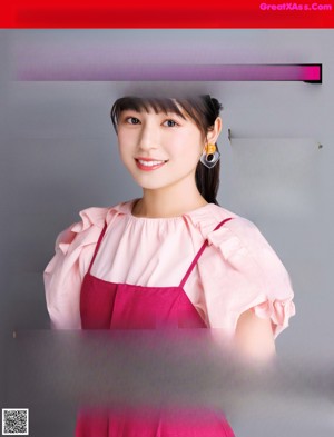 A woman in a pink dress is standing in front of a gray background.