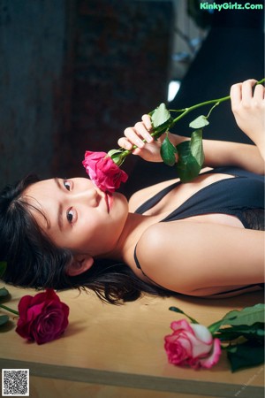 A woman in a black bathing suit holding a bouquet of flowers.