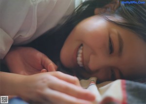 A woman in a blue sweater sitting on a bed.