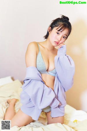 A woman in a blue sweatshirt is sitting on a bed.