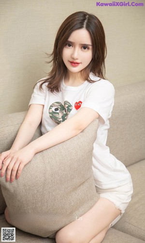 A woman sitting on a couch wearing a white shirt and shorts.